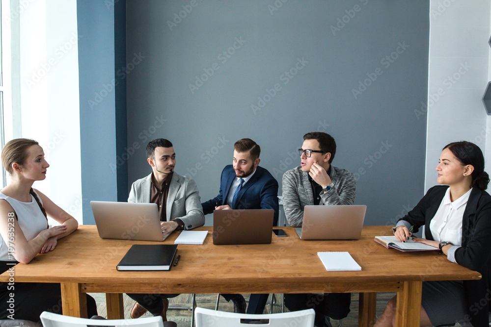 Business team of five people sitting with laptops at the table in the office Business team of five people sitting with laptops at the table in the office