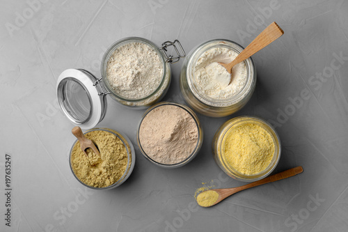 Jars with different types of flour on gray background