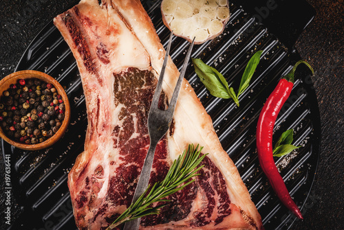 Raw beef marbled meat striplon rib eye steak with spices, grill pan, and herbs, dark background top view, copy space photo