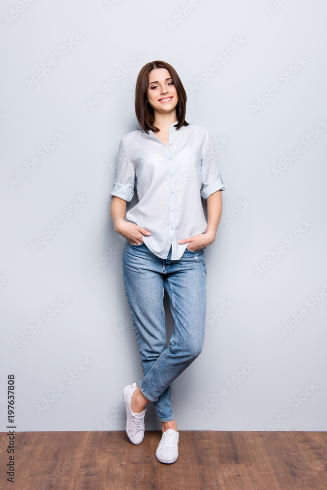 Vertical full length fullbody portrait of trendy, cheerful girl in denim, casual outfit, standing leg by foot, lean on wall, holding hands in pocket, looking at camera, isolated on grey background Vertical full length fullbody portrait of trendy, cheerful girl in denim, casual outfit, standing leg by foot, lean on wall, holding hands in pocket, looking at camera, isolated on grey background