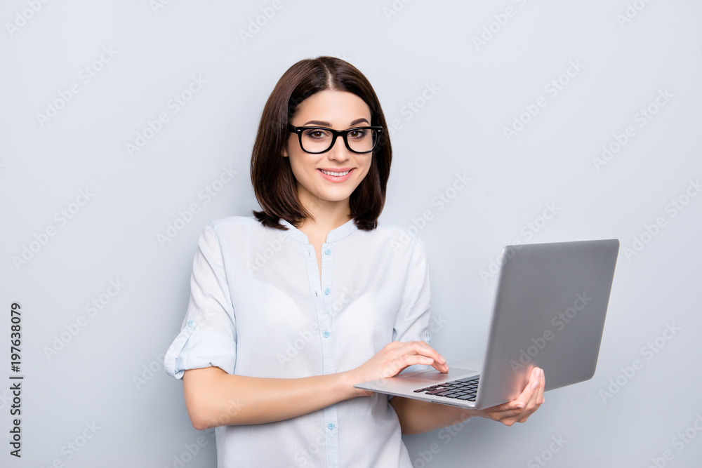 Portrait of pretty, charming, stylish, clever woman with modern hairstyle having open laptop in hands, texting email, chatting, using wifi internet, looking at camera, isolated on grey background Portrait of pretty, charming, stylish, clever woman with modern hairstyle having open laptop in hands, texting email, chatting, using wifi internet, looking at camera, isolated on grey background