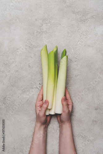 cropped shot of person holding fresh healthy leeks on grey