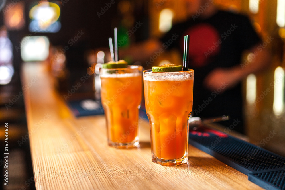 Close-up of two colorful orange cocktails with lime and brown sugar in bar, blurred background.