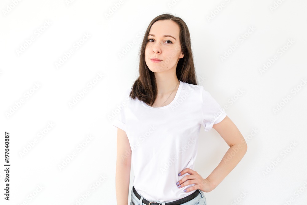 Young brunette girl stands on white background with her hand on her waist Young brunette girl stands on white background with her hand on her waist