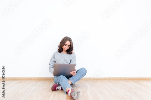 Young girl sitting in an empty room sitting on the floor with a laptop