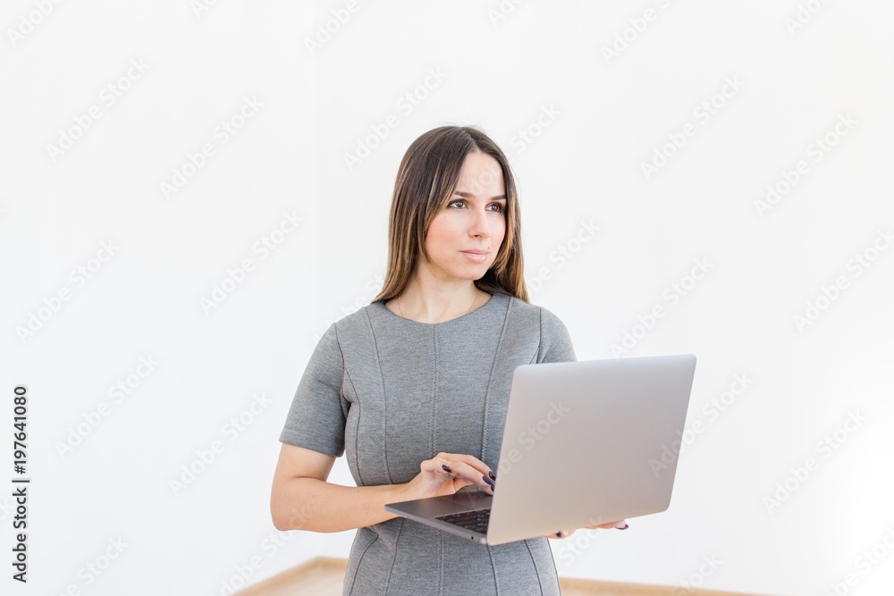 Woman in gray dress standing with laptop in hands on white background Woman in gray dress standing with laptop in hands on white background