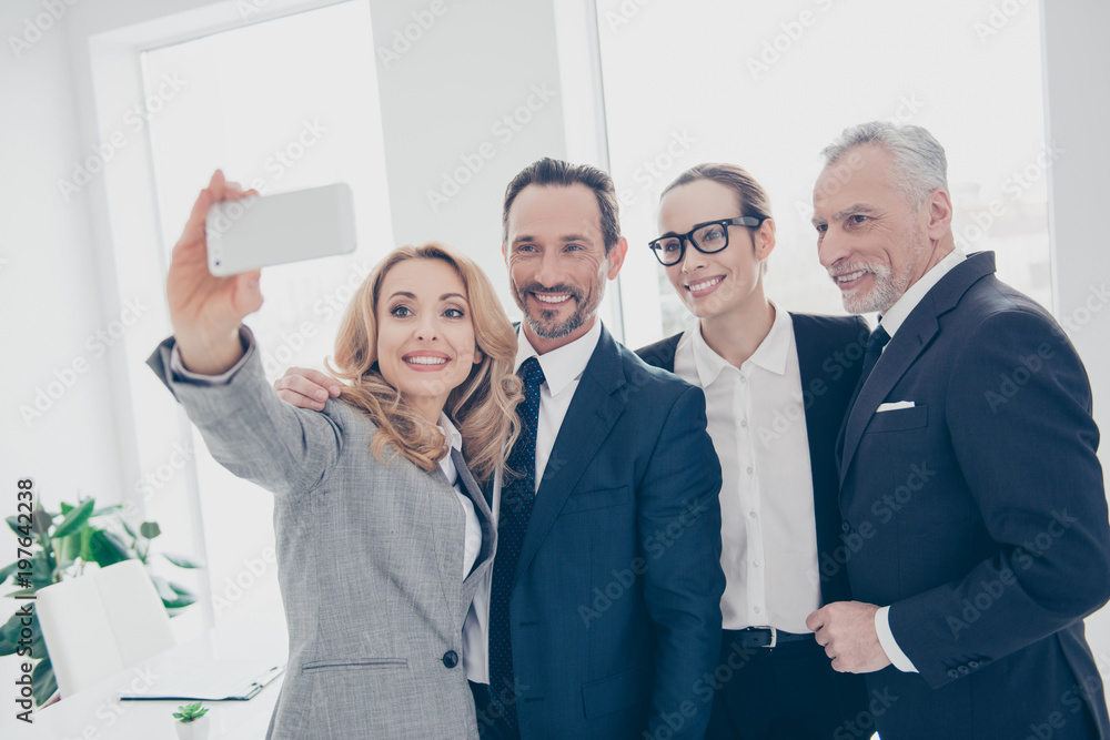 Portrait of attractive, cheerful, stylish, confident business persons standing in work place, station, shooting selfie on front camera, using smart phone, having break, pause, time out