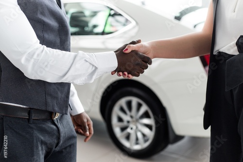 Handshake closeup of African men with the girl in the showroom on the background of a new car © pantovich