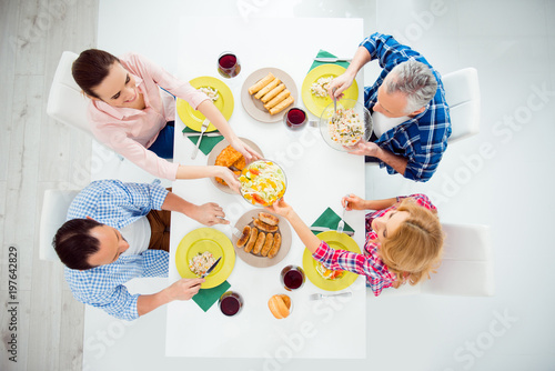 Top view portrait of festive stylish attractive relatives imposing food in plates, eating with knife, fork, sitting in house, apartment, room, having meat, salads and glasses of red wine on the table photo