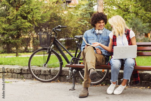 Young cheerful couple sitting on the bench studying together in the park