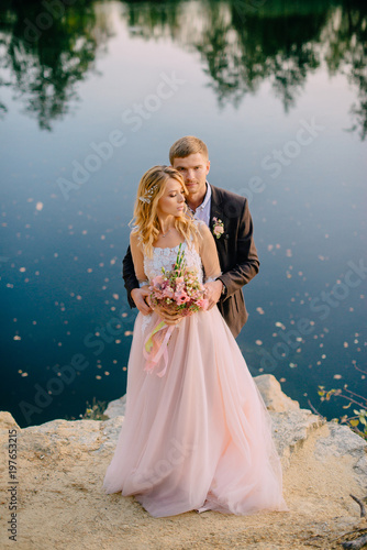 happy newlyweds standing against nature background at sunset