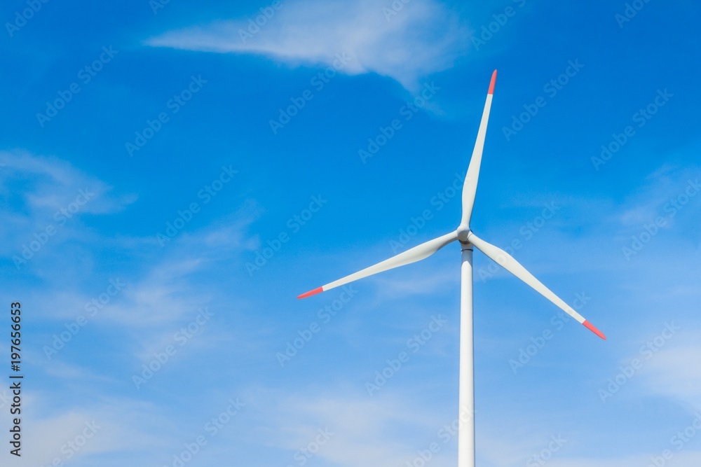 Rotating windmill generating renewable energy with wind power. Sustainability by windmills turbines preventing climate change with regenerative clean green nature energy. Windy blue sky with clouds