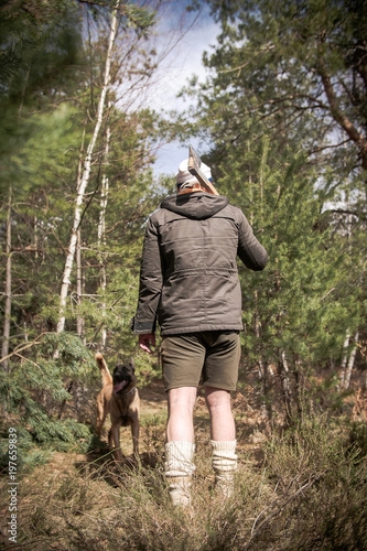 Handsome Man Lumberjack and his Belgian Shepherd Posing in Front of a Camera With Mountains In The Background