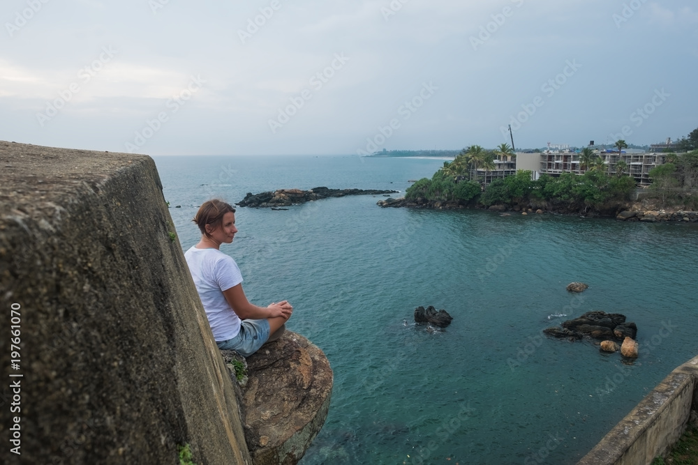 caucasian woman sitting on stone of fortress in Galle Sri lanka. It is very high. Ocean is seen on the background