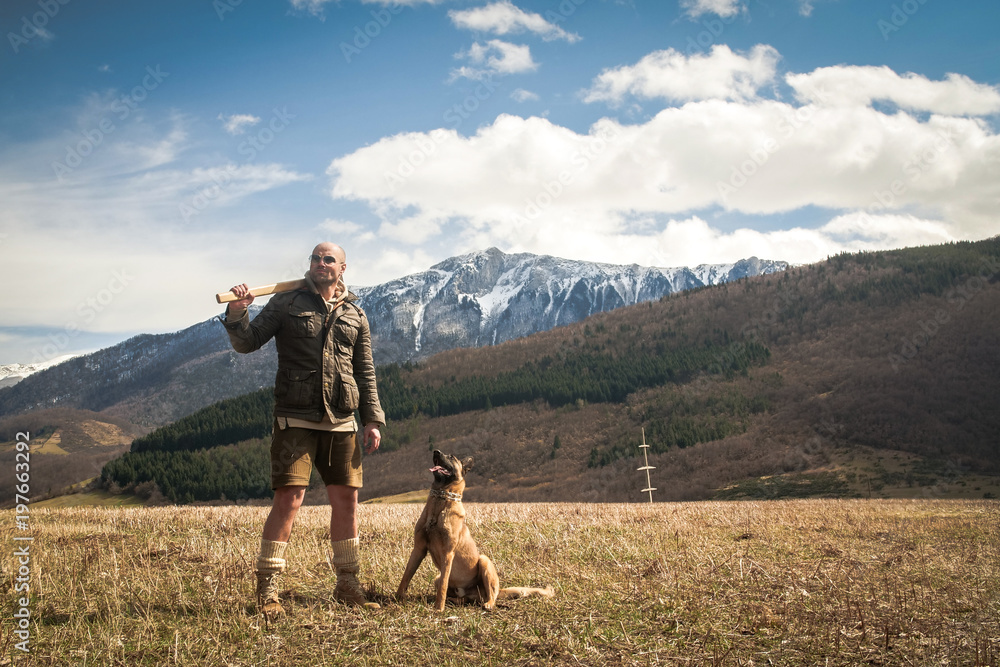 Handsome Man Lumberjack and his Belgian Shepherd Posing in Front of a Camera With Mountains In The Background Handsome Man Lumberjack and his Belgian Shepherd Posing in Front of a Camera With Mountains In The Background