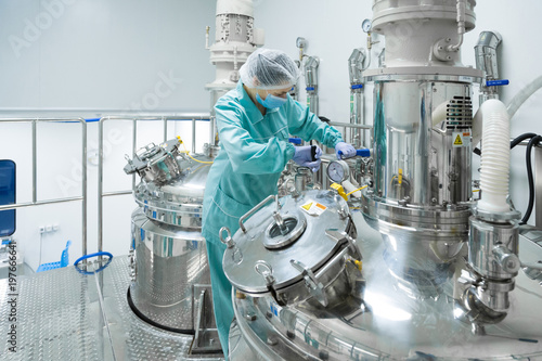 Pharmaceutical factory woman worker in protective clothing operating production line in sterile environment photo