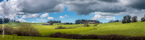 A panoramic of green pastures with a barn and cows grazing in the distance. Fluffy white clouds with darker ones threaten rain. photo