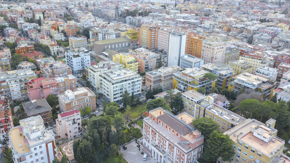Aerial view of a group of buildings in the Prati district in Rome, city e capital of Italy. The roofs are passable and with antennas and TV. down the sun lit streets there are cars and trees.