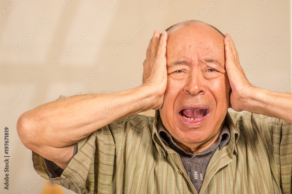 Portrait of a worry mature man holding his head with both hands, in a blurred background Portrait of a worry mature man holding his head with both hands, in a blurred background