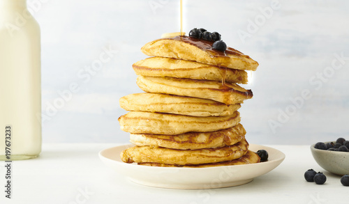Stack of pancakes with blueberries and maple syrup in plate on table photo