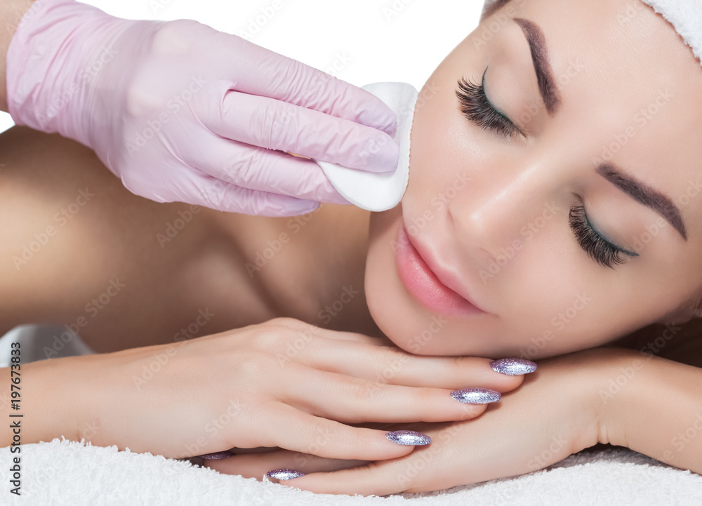 The doctor cosmetologist cleanses with a tonic the face skin of a beautiful, young woman in a beauty salon.Cosmetology skin care. The doctor cosmetologist cleanses with a tonic the face skin of a beautiful, young woman in a beauty salon.Cosmetology skin care.