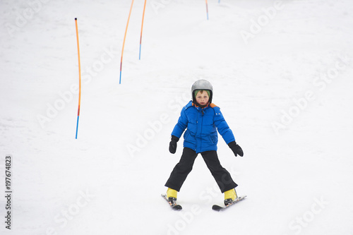 Child boy skiing in winter mountains. Active kid with safety helmet and goggles. Ski race for young children. Winter sport for family. Kids ski lesson in school. Young skier racing in snow