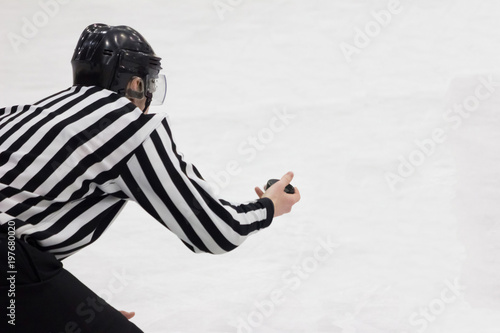 Hockey referee holding a puck in face off position. Back view. White background, isolated.