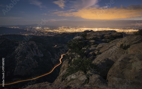 Light trails of vehicles descending the mountain at night are shown. Tucson city lights are in the background.