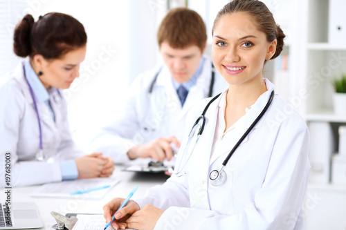 Wallpaper Mural Happy female doctor keeping medical clipboard while medical staff are at the background Torontodigital.ca