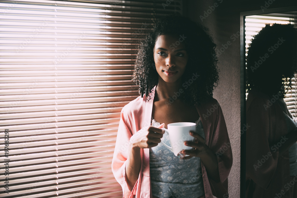 Obraz premium pretty black woman standing at the window with cup of coffee