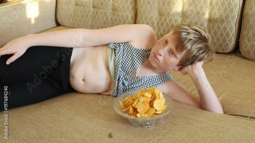 Fat boy eats chips on a sofa
