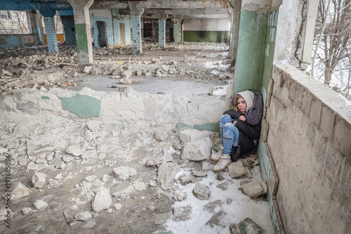 little girl teenager sitting and sleeping on the floor of a ruined building in the war