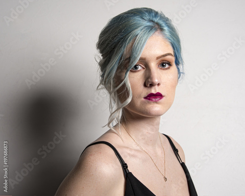 BIRMINGHAM,UK - FEBRUARY 2018: Caucasian female model, Age 22, Blue dyed hair, Red lips, black strappy top,Isolated on mid grey background. Head and shoulders photo