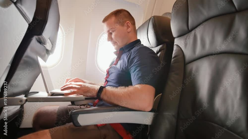 A young man was sitting on the plane and working on his laptop before departure. A young man was sitting on the plane and working on his laptop before departure.