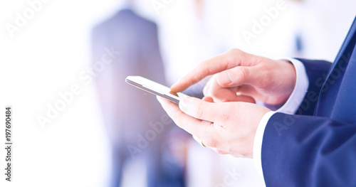 Portrait of young businessman in office with colleagues in the background and using mobile