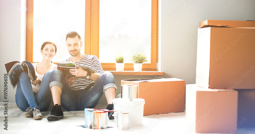 Attractive couple sitting on home floor looking at jurnal and smiling at each other. Attractive couple sitting on home floor looking at jurnal and smiling at each other.