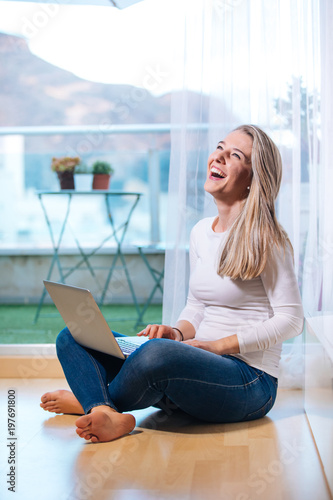 Free Download relaxed smiling barefoot woman sitting on the floor looking at her laptop - GFXLoad