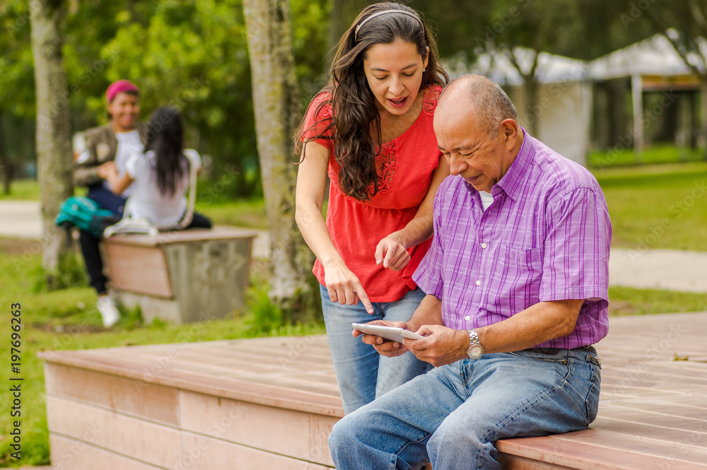 Fototapeta premium Outdoor view of father and daughter using a cellphone in the park