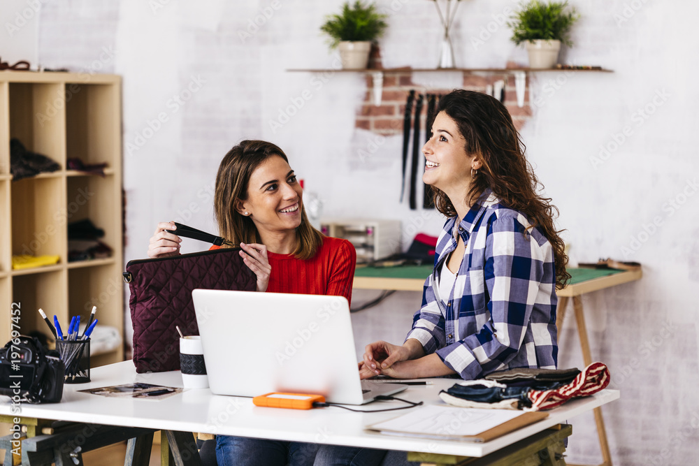 Two smiling fashion designers working in studio with laptop Two smiling fashion designers working in studio with laptop
