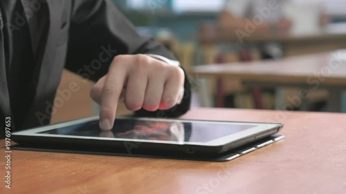 Close-up of hand of student boy dressed in black suit sits at desk at office the resting and looking at favorite photos using the screen of computer tablet in white-black colour. photo