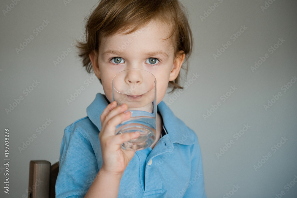 Cute little boy in blue shirt drinks water from a glass.