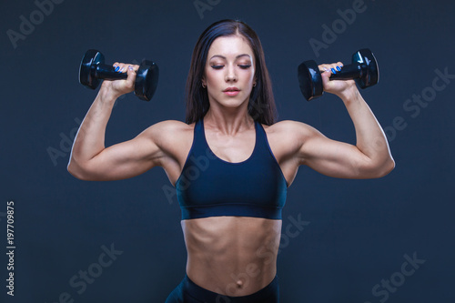 Brutal athletic sexy woman pumping up muscules with dumbbells. The concept of exercise sports, advertising a gym.