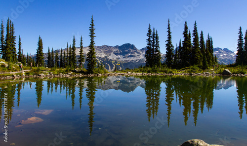 A beautiful summer landscape view of Blackcomb mountain viewed from Whistler on a hiking trail by harmony lakes with people walking on the boardwalk in the distance