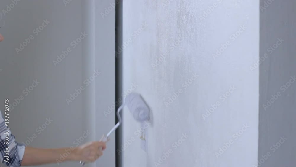Young woman painting wall in white with paint roller Young woman painting wall in white with paint roller