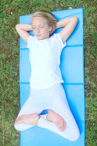 School-age girl has a rest and goes in for sports, she lies with her eyes closed, on the mat in the park. Yoga and relaxation.