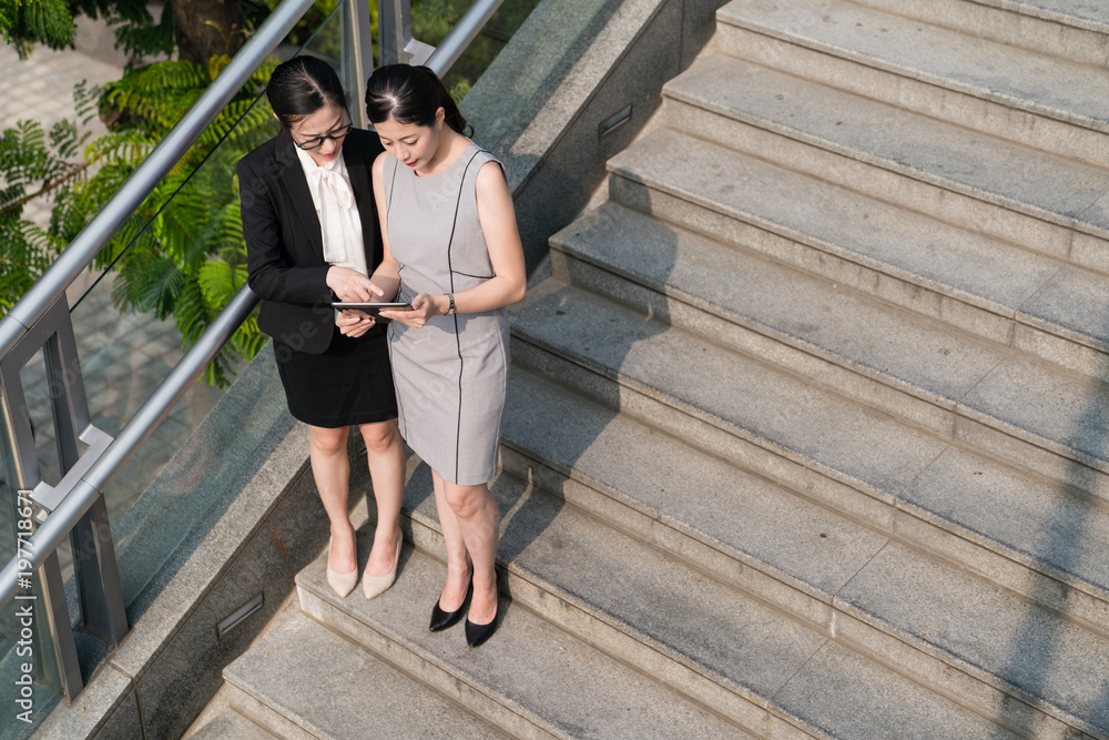 businesswomen standing on stairs using a tablet.