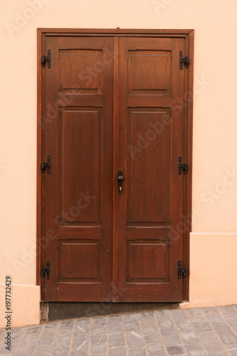 Old brown door on beige wall. House exterior details and decoration.