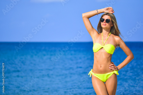 beautiful fit young woman in sexy yellow bikini at the beach and blue sea