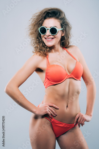 Young woman in sunglasses with beautiful slim perfect body in bikini isolated gray background © F8  \ Suport Ukraine