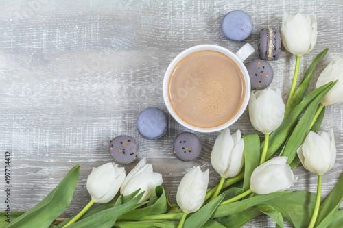 Cup of coffee, white tulips and gray macaroons on light wooden surface